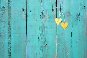 Two gold hearts hanging on antique teal blue wood fence