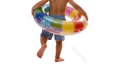 Child walks forward carrying colorful inflatable swim ring during summer