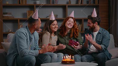 Four multiracial friends celebrating birthday party presenting present Caucasian woman receive gift from diverse