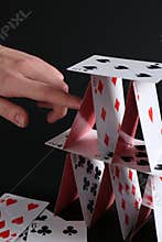 Woman destroying house of playing cards on black background, closeup