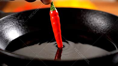 Red Chili Pepper About to Drop Into Hot Oil in Cast Iron Pan