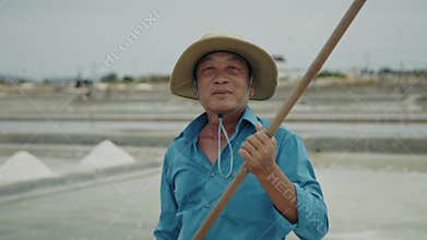 Portrait of happy senior Asian man with wooden shovel at solar evaporation pond