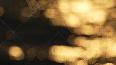 blurry, yellowish-orange sunset over water. The water appears to be rippling and the sky is filled with a warm, golden glow.