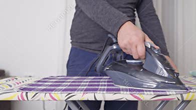 A Person Carefully Irons a Purple Checkered Cloth on a Patterned Ironing Board