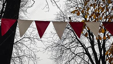 Red and white triangular bunting hanging against a background of bright yellow autumn foliage and sky