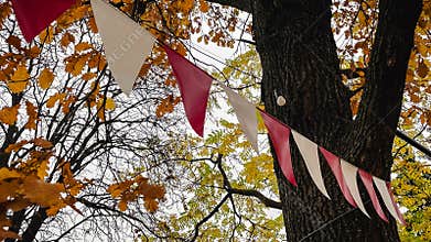 Red and white triangular bunting hanging against a background of bright yellow autumn foliage and sky