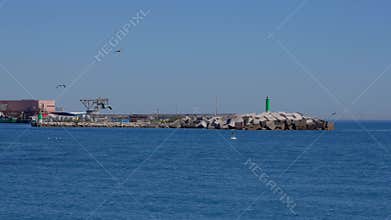 Green beacon standing on concrete blocks protecting harbor entrance from waves - MARBELLA, SPAIN - MARCH 30, 2025