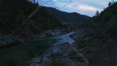 Mountain river with rocky shores and arched bridge at sunset