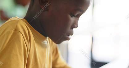 Teenage male typing on white laptop at desk, leaning and reading screen while finishing assignment