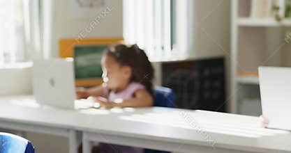 Camera shifting focus is revealing curly-haired girl typing on laptop in class to finish assignment