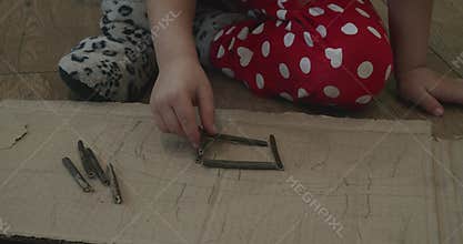 Little girl's hands constructing a small square shape with wooden sticks while sitting on the floor. Early childhood
