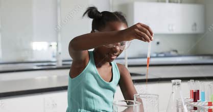Plastic pipette is dropping orange drops into beaker while being lowered for school lab transfer
