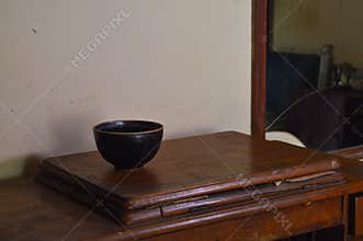 A Small Black Ceramic Bowl Placed On The Left Side Of An Old Wooden Desk