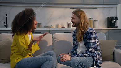 Happy excited multiethnic couple amazing news at home talking couch Caucasian man surprised listening talk African