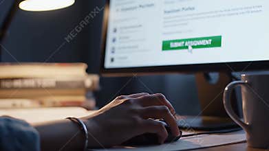 Hand clicking \'Submit Assignment\' on computer screen, late night study.