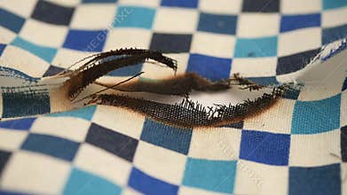 Checkered fabric with burn marks and frayed edges