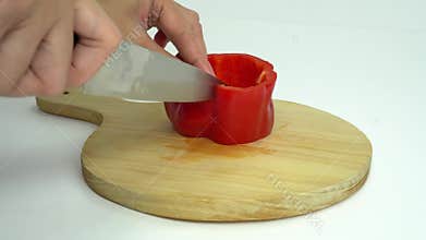 A woman is cutting the body of a red bell pepper or red paprika into 3 parts, on a round brown wooden cutting board