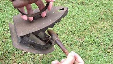 Close Up of Hand Cleaning Antique Charcoal Iron with Brush on Green Grass