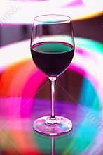 Glass of red wine on a table with colorful light patterns in the background during evening time