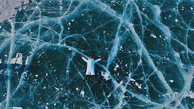 Aerial View of Person Lying Down on Frozen Turquoise Ice with Cracks in Winter