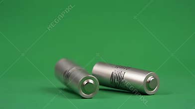 Two silver cylindrical batteries lie side by side on a vibrant green background, symbolizing portable energy and sustainable power