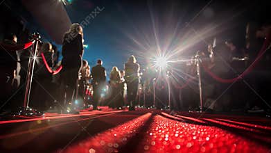 Low angle view of a glittering red carpet with celebrities and paparazzi. Flashing lights and photographers capture a glamorous