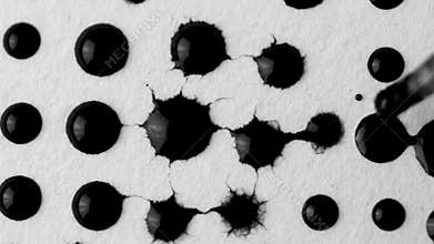 Black ink drops spreading on white textured paper, creating abstract patterns for design.