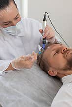 Trichologist doing man hair regeneration procedure dermapen microneedling vitamin exosomes injection
