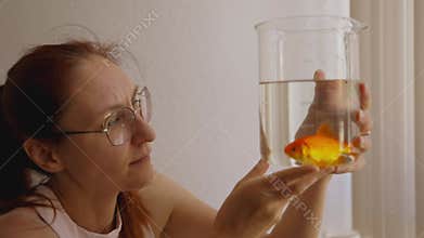 Curious woman examining goldfish in glass beaker