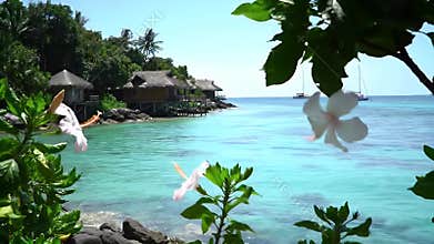 Sunlit tropical ocean scene with turquoise waters, lush greenery, and distant thatch-roof bungalow resorts