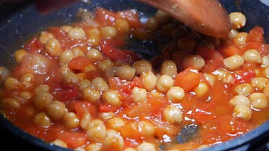 Cooking chickpeas with tomatoes in a pan on a stove