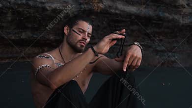 A young, handsome and courageous European man with drawings on his body sits on black sand