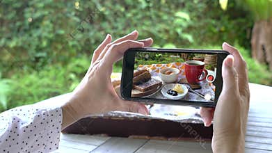 Woman taking video using her cellphone of her breakfast.