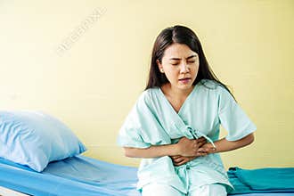 Woman patient  suffering from stomach ache while sitting on bed at hospital, abdominal pain, food poisoning