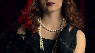 Woman dressed in style of Great Gatsby demonstrates jewelry and bijouterie of that time on hands and dress. Roaring