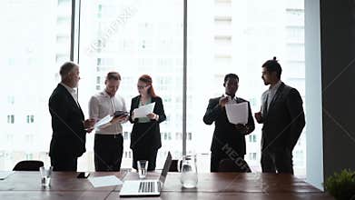 Successful multi-ethnic business team of businessmen and businesswoman reviewing documents by window