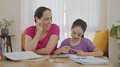 Mother helping her young daughter prepare homework during homeschooling