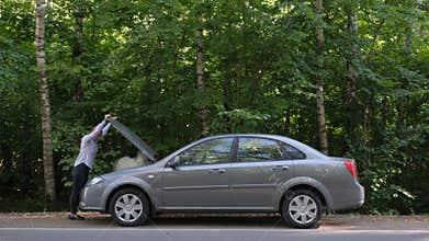 A young woman a broken car and opens the hood in the forest. The car suddenly broke down on a country road down while