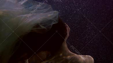 Sensual man and woman are underwater in darkness, swimming and caressing, lovers in pool