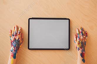 Close up view of designer workplace with blank screen tablet and painter`s hands in paints, top view