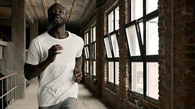 Fit black man in sport wear running near windows indoors
