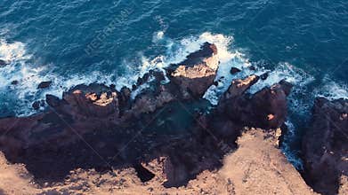Drone flying along rocky beach. Beautiful coastline with waves. Aerial view of big sea rocks. Top view of big waves