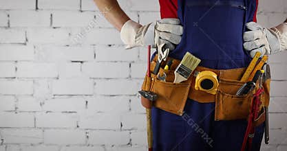 Construction worker with tool belt standing on white brick wall background