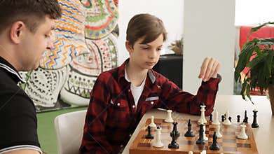Happy teenage kid is laughing winning his father in chess front view slow motion