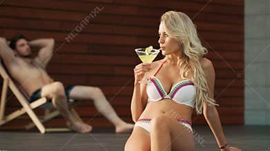 Flirting woman drinking cocktail near swimming pool. Modern couple relaxing