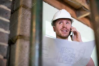 Architect Inside House Being Renovated Studying Plans Talking On Mobile Phone