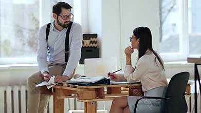 Happy young male manager businessman talking to female boss colleague sitting on table at comfortable modern loft office