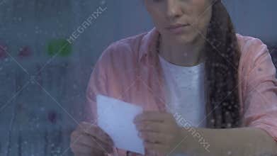 Upset young female holding family photo near rainy window, suffering divorce