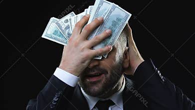 Greedy business man stroking face with dollars banknotes, enjoying wealth