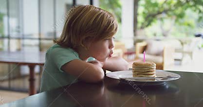 Boy blowing candle on pancake at dining table in kitchen at home 4k